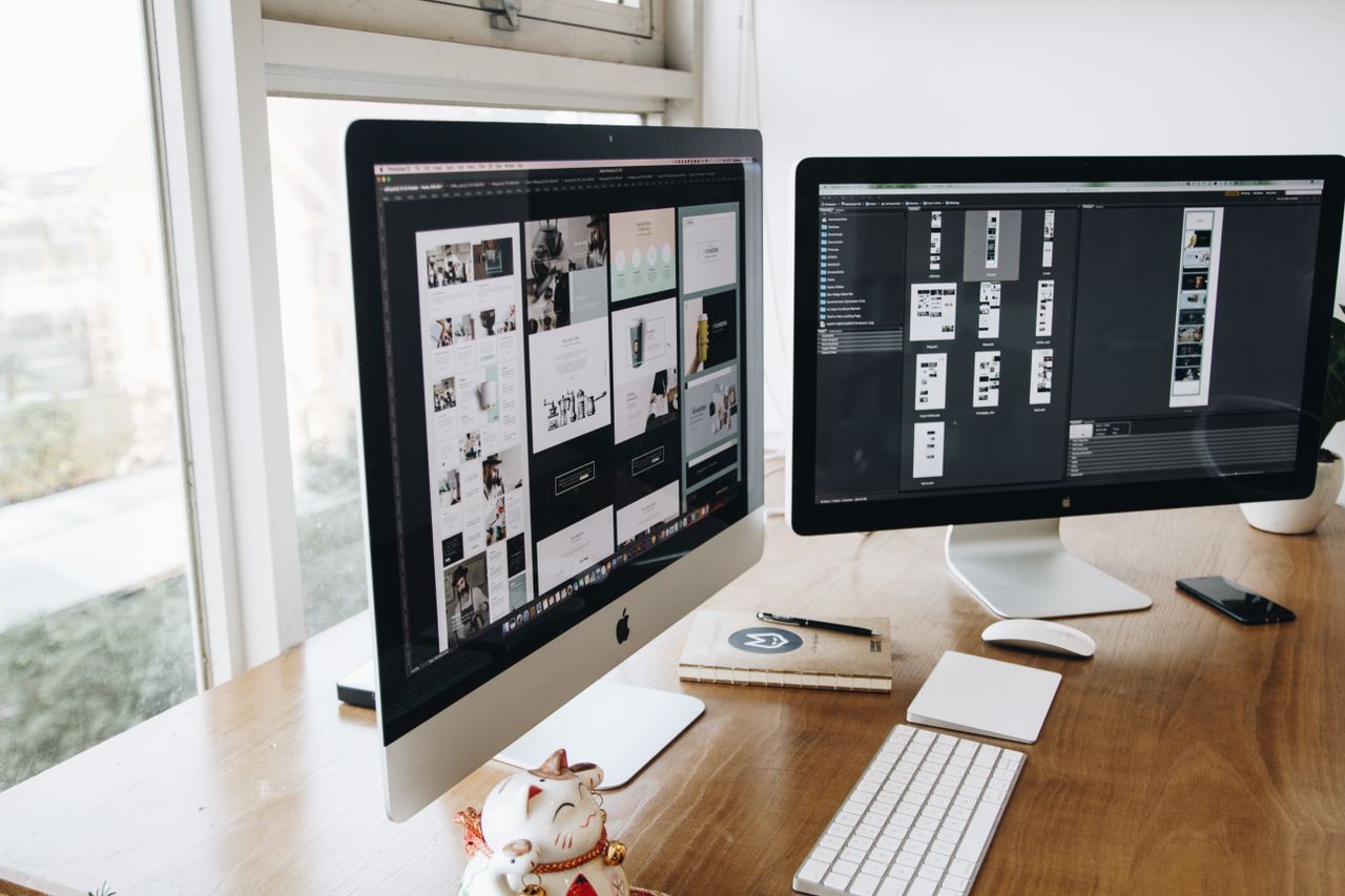 A digital workspace featuring dual monitors, keyboard, mouse, and decor on a wooden desk.